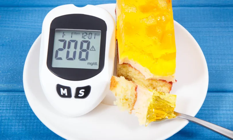 Glucose meter showing 208 mg/dL beside a slice of cake with a fork.