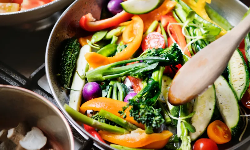 Cooking colorful chopped vegetables in a pan with a wooden spoon.