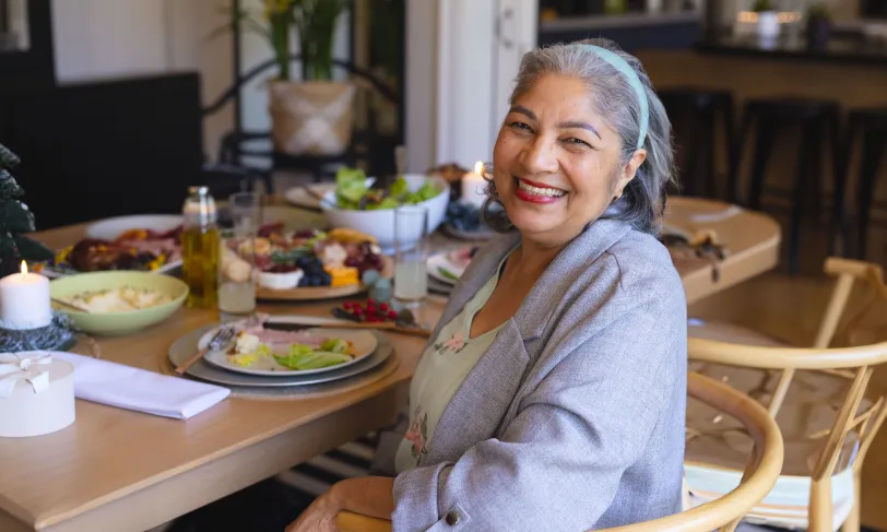 Joyful older woman at a dining table with healthy meal options.