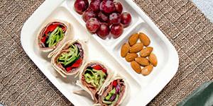 A lunch tray with wraps, almonds, and grapes. 