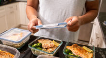 A pair of hands add a lid to meal prepped dinners