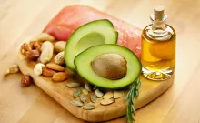 A wooden board with healthy fats like avocado, olive oil, and nuts for a healthy diet.