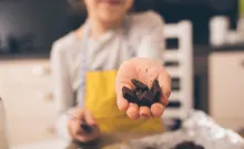 A person cutting up dark chocolate and offering it towards the camera