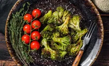 Roasted broccoli, cherry tomatoes, and herbs on a dark plate.