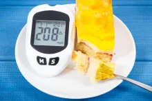 Glucose meter showing 208 mg/dL beside a slice of cake with a fork.