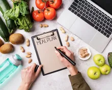 a first person view of a person writing on a clip board with some fresh fruits and vegetables surrounding it. 