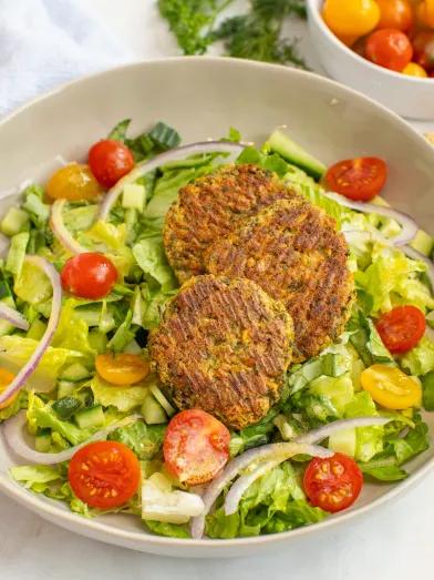 salad with three falafel patties, lettuce, cherry tomatoes, cucumber, and red onion in a bowl.