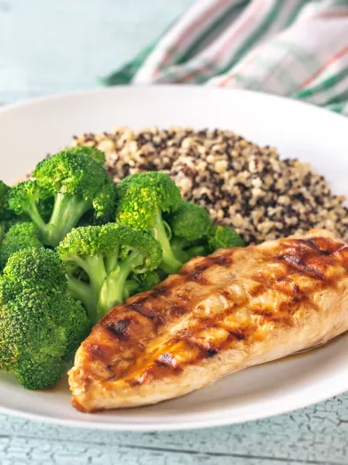 Grilled chicken, broccoli, and quinoa on a white plate.
