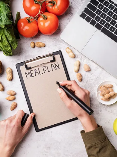 a first person view of a person writing on a clip board with some fresh fruits and vegetables surrounding it. 