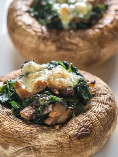Two stuffed mushrooms with spinach and melted cheese on a white plate.
