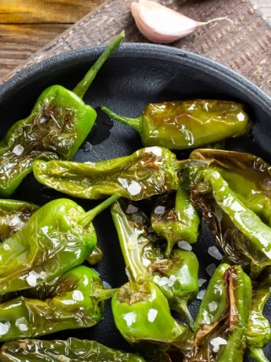 Blistered green peppers with sea salt in a black pan