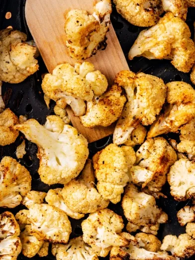 Golden-brown roasted cauliflower in a baking pan, with a wooden spatula.