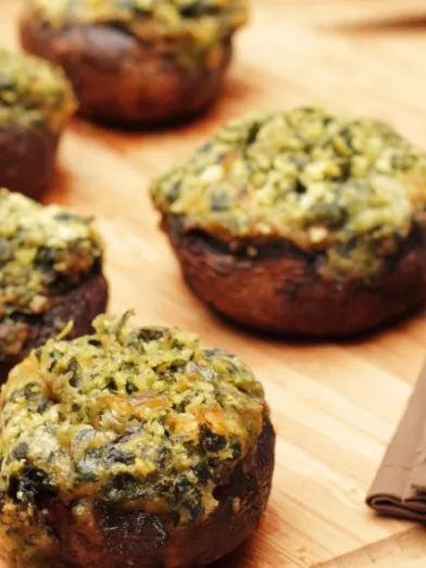 Five stuffed mushrooms with spinach and feta on a wooden board, a fork nearby.