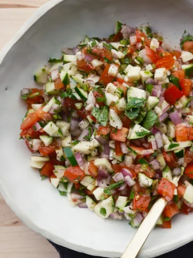 Fresh salsa with diced tomatoes, zucchini, onions, and herbs in a white bowl, with lime.