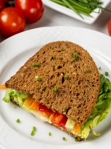 Sandwich on wheat bread with lettuce, colorful bell peppers, hummus