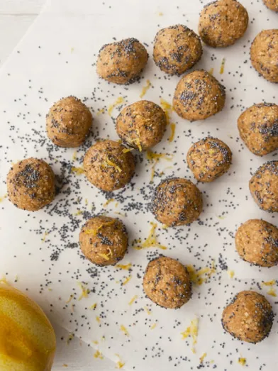 Lemon poppy seed energy bites on parchment paper with a fresh lemon.