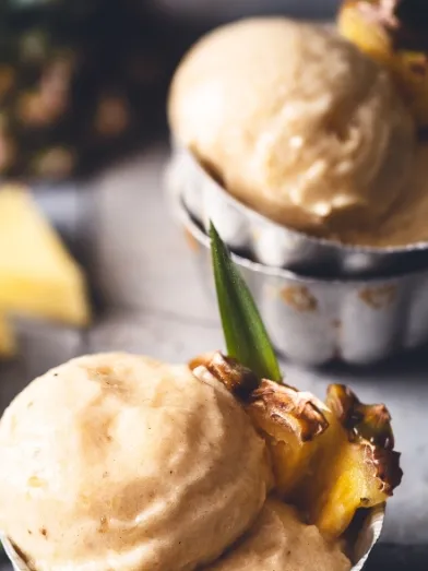 Scoops of light yellow pineapple frozen dessert garnished with fresh pineapple pieces.