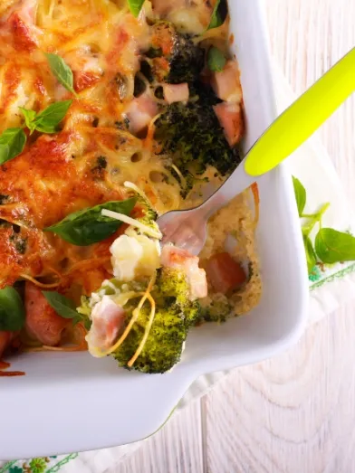 Cheesy broccoli and ham casserole in a white dish, with a serving fork.