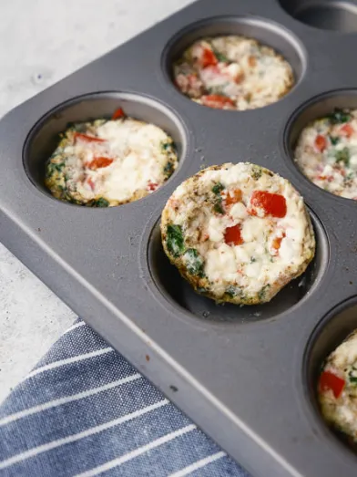 Healthy egg bites with red pepper and greens in a muffin tin.