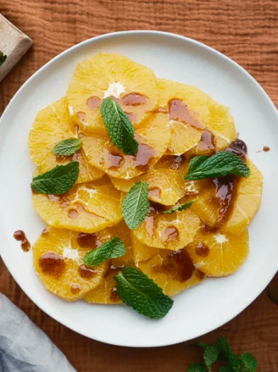 Fresh sliced oranges with mint and drizzle on a white plate. Spices nearby.