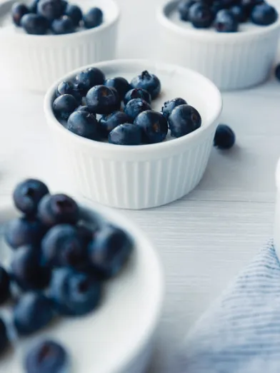 Small white bowls of yogurt mousse topped with fresh blueberries on a light surface.