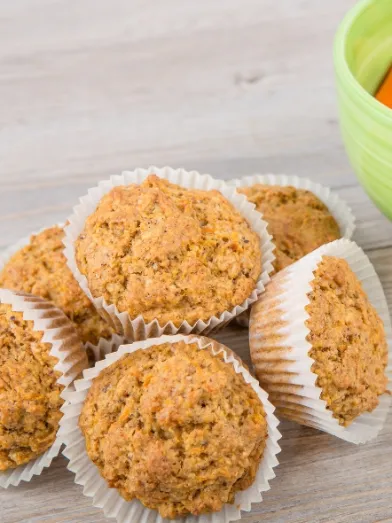 Muffins in white liners next to a green bowl of baby carrots.
