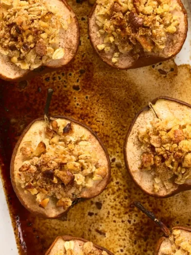 Halved baked pears with golden oat and nut topping in a white baking dish.