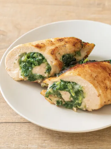 Two baked chicken breasts, sliced to show a green spinach filling, on a white plate.