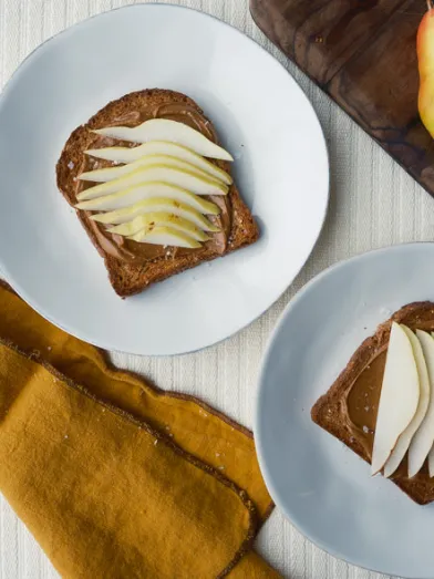 Toast with spread and sliced pears on white plates; whole pears on a board.