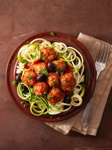 Plate with zucchini spaghetti, meatballs, tomato sauce, and black olives.