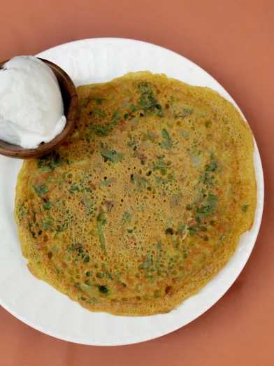 Savory pancake on a white plate with a side of yogurt.
