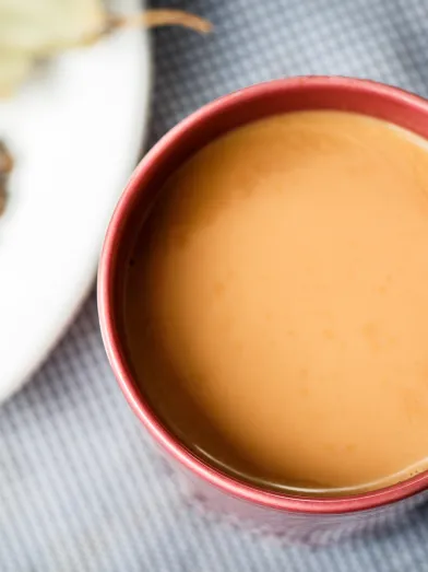 Chai tea in a red mug next to a plate of dried spices.