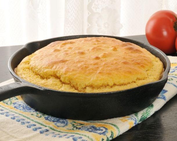 Cornbread in an iron cast skillet with tomatoes on top of a towel.