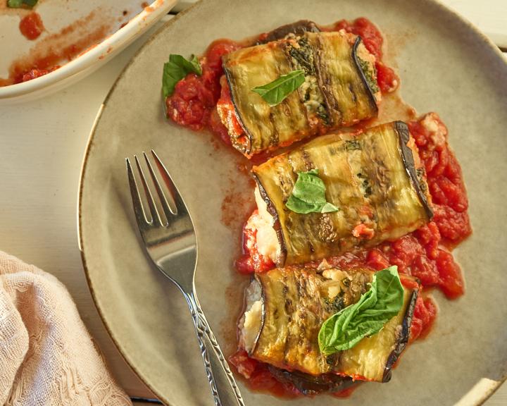 Eggplant rolls served on a plate with tomato sauce.
