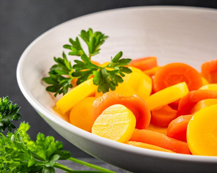 steamed yellow and organge carrot slices in bowl with parsely