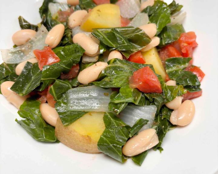 A plate of cooked collard greens, white beans, and potatoes. 