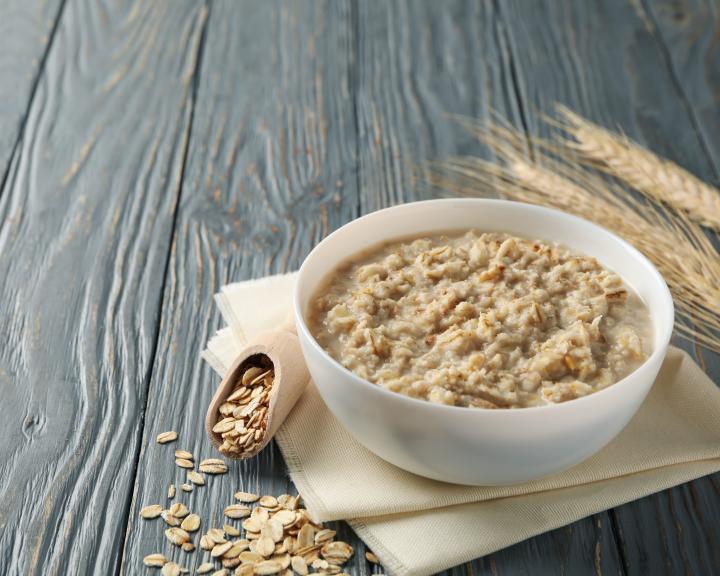 Bowl of oatmeal, scattered oats, wooden scoop, and wheat on a rustic grey table.