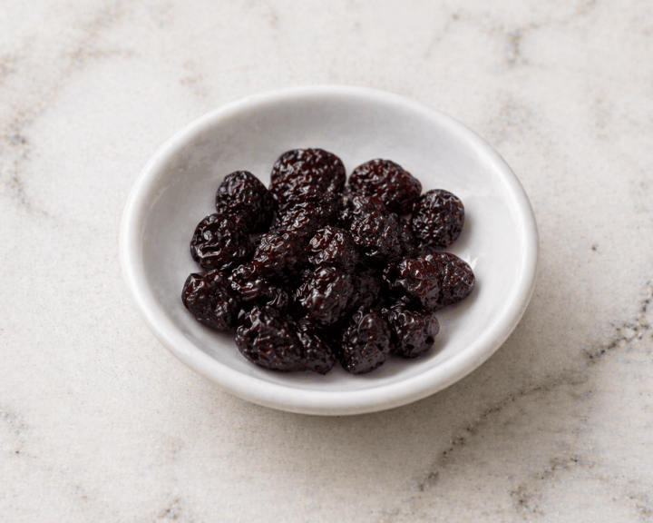 2 Tbsp of unsweetened dried cherries in a small white bowl on a marble surface. 