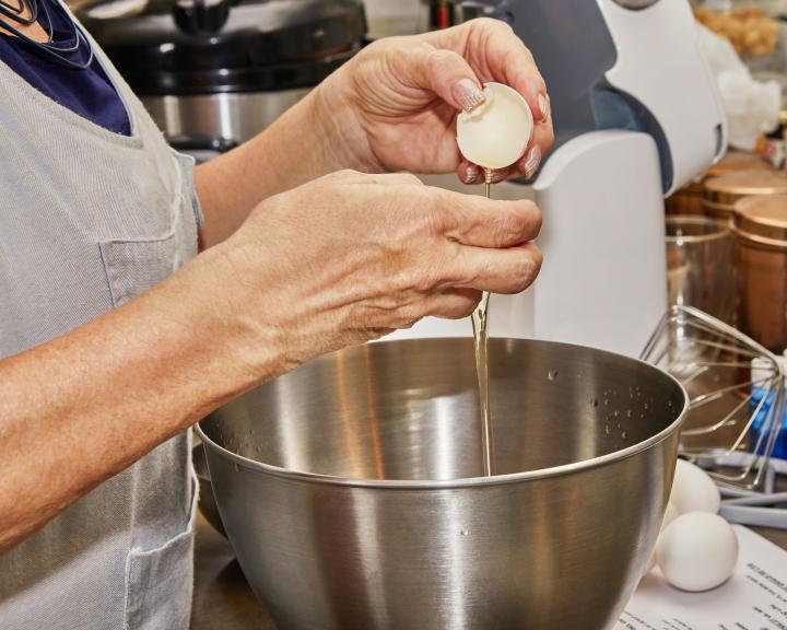Woman cracking an egg to get egg white into stainless steel bowl for cooking