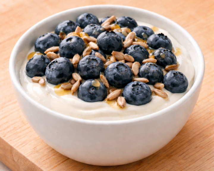Bowl of yogurt topped with fresh blueberries, sunflower seeds, and a drizzle of honey.