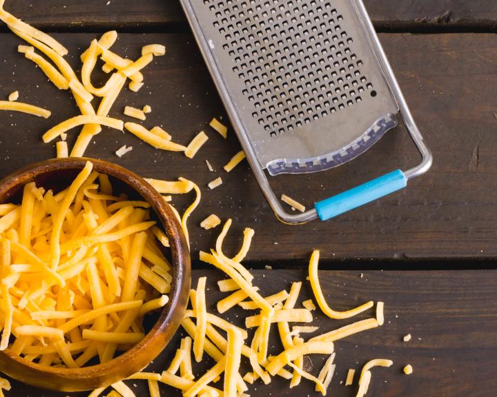 shredded low-fat cheddar cheese on wooden table next to grater