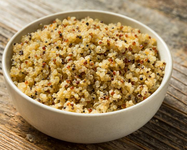 Bowl of cooked multi-colored quinoa on a wooden table.