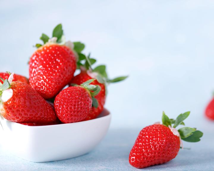 Bowl of fresh red strawberries on a light blue surface.