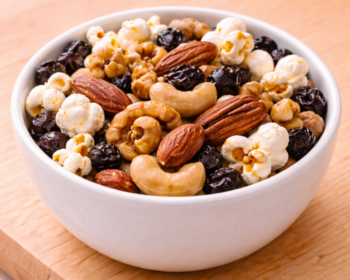 Small white bowl with a mix of popcorn, mixed nuts, and raisins