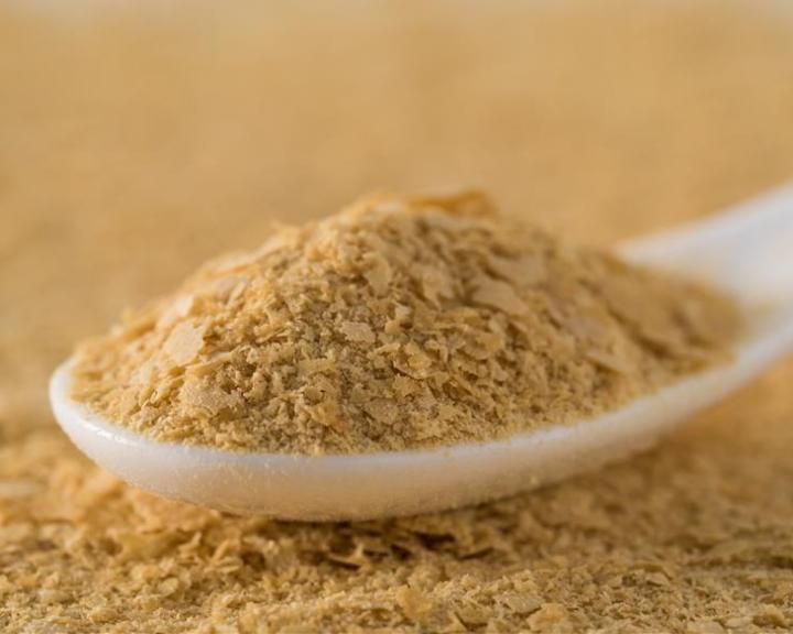 White spoon holds a mound of light brown nutritional yeast flakes.