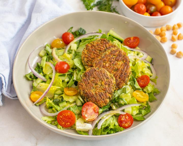 salad with three falafel patties, lettuce, cherry tomatoes, cucumber, and red onion in a bowl.