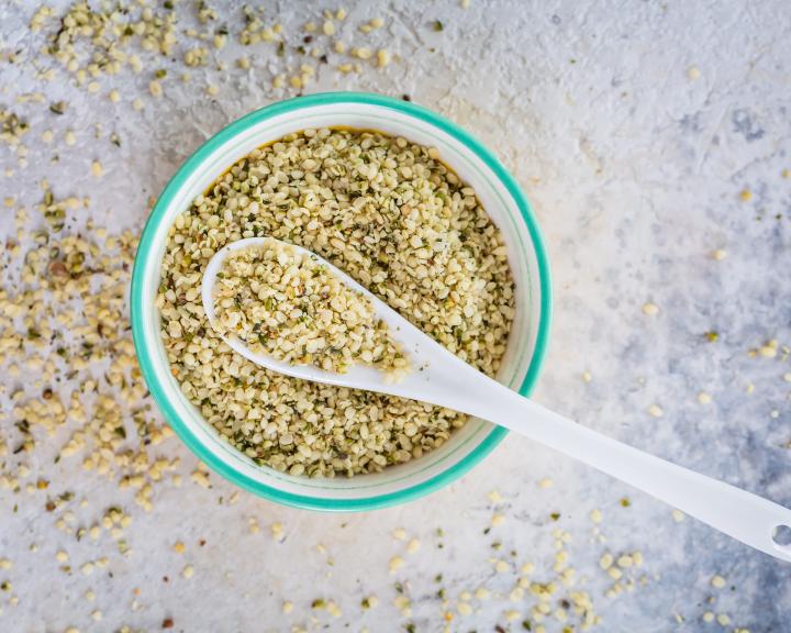 Bowl of hemp seeds with a white spoon on a light gray surface.