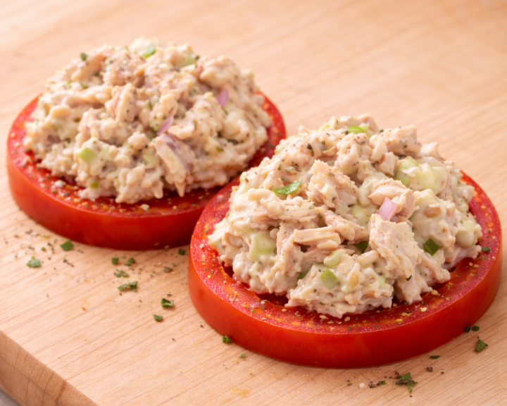 Healthy tuna salad on two tomato slices, sprinkled with herbs.