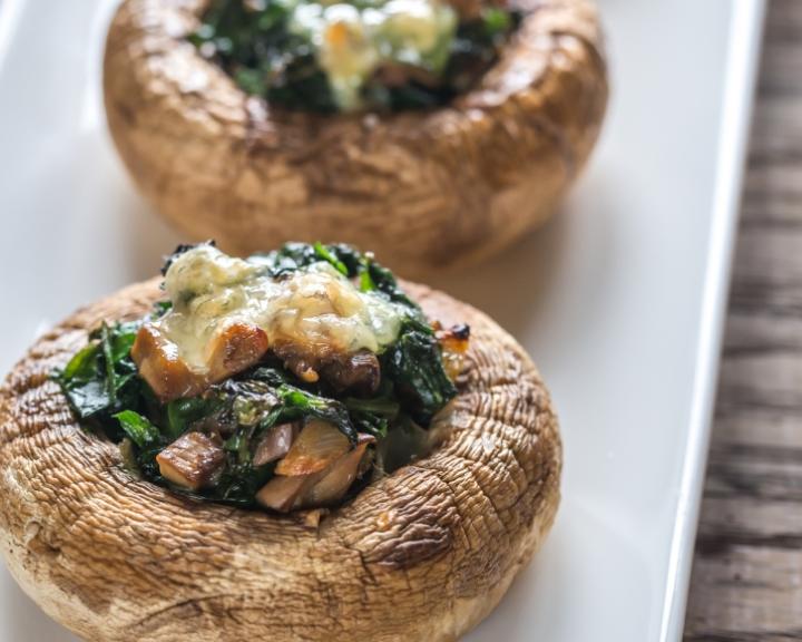 Two stuffed mushrooms with spinach and melted cheese on a white plate.