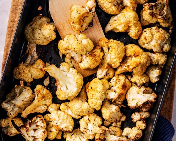 Golden-brown roasted cauliflower in a baking pan, with a wooden spatula.